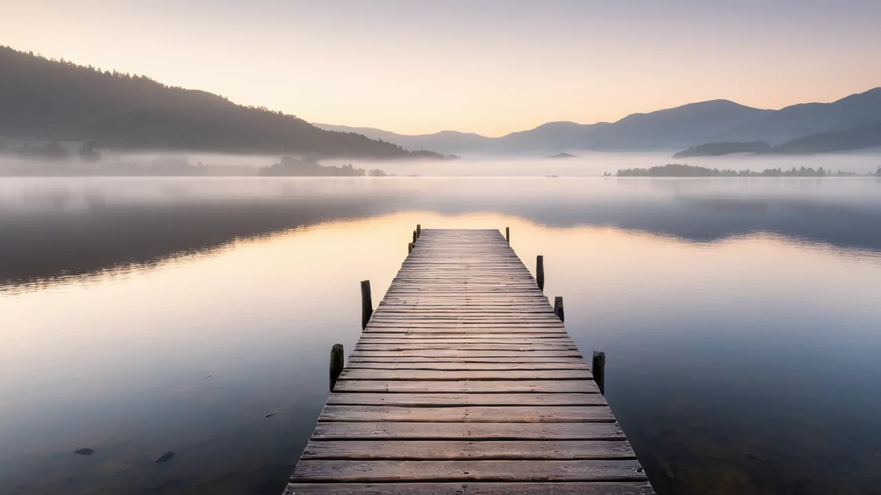 A still lake at dawn, with low fog over the water and an empty wooden jetty.